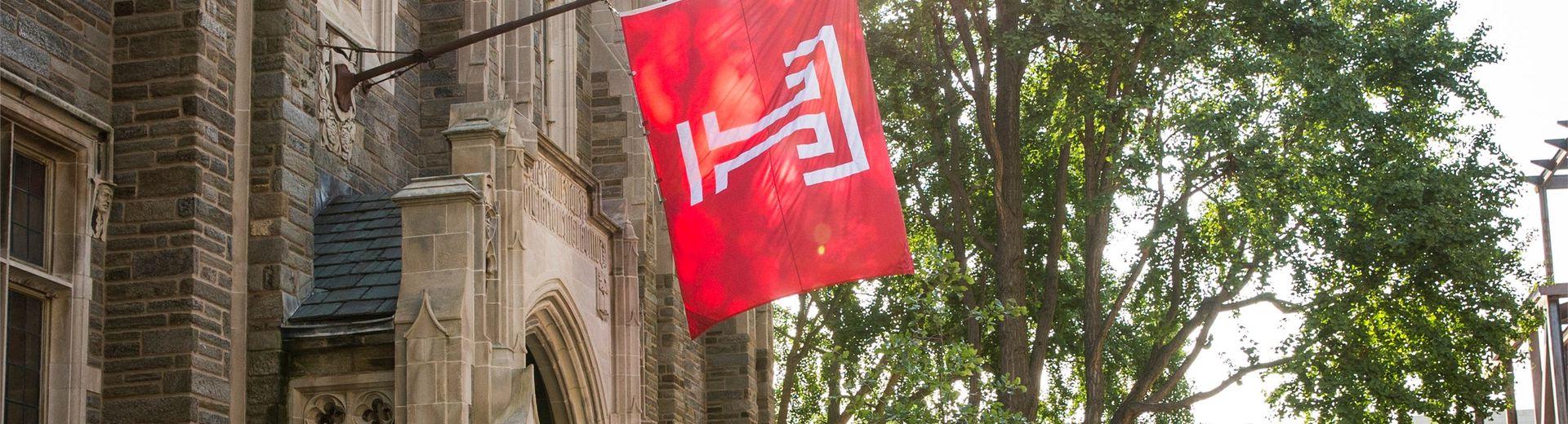 亿德体育 flag hangs from a historic building on campus.